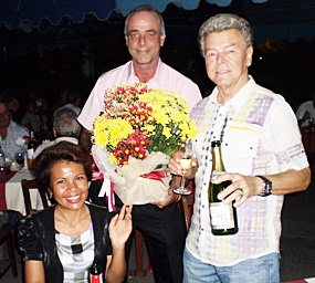 Andy Wenger (center) receives flowers from Horst Filla (right), House & Apartment Contractor, and his lovely wife Pantaree.