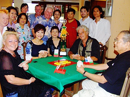 Members of both bridge teams pose for a photo around a game table supporting the honorary trophy.