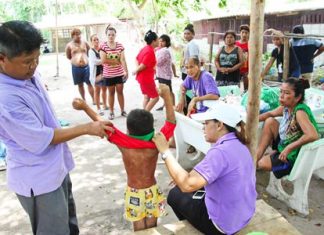 Malai Wattananon (seated, far right) looks on as officials inspect cuts to the neck, face and legs on her 11-year-old grandson who she had been beating mercilessly with a wire nearly every day. She has been arrested and charged with child abuse.