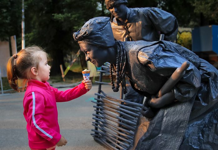 In this Thursday, May 24, photograph, a child offers ice-cream to artists of Ukraine’s Artel Myth theatre at the Living Statues International Festival, in Bucharest, Romania. (AP Photo/Vadim Ghirda)