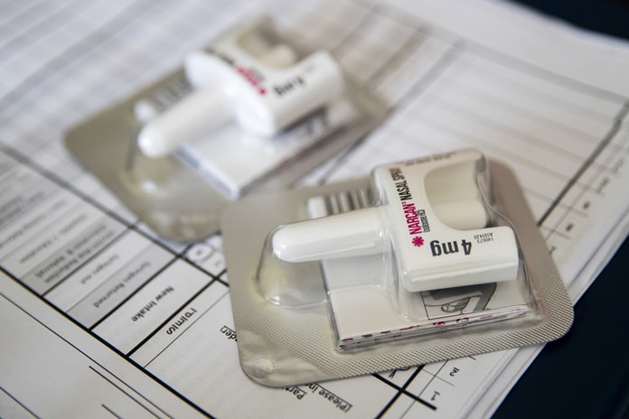 In this Tuesday, July 3, 2018 file photo, a Narcan nasal device which delivers naloxone lies on a counter as a health educator gives instructions on how to administer it in the Brooklyn borough of New York. On Wednesday, Dec. 19, 2018, the U.S. government told doctors to consider prescribing the overdose antidote naloxone to many more patients who take opioid painkillers. (AP Photo/Mary Altaffer)