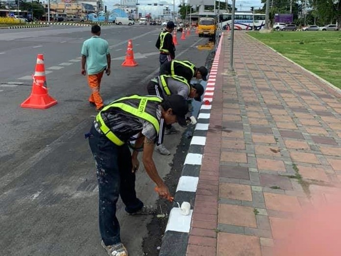 Workers paint red and white stripes on the curb which means, ‘Strictly No Parking’ at all times.