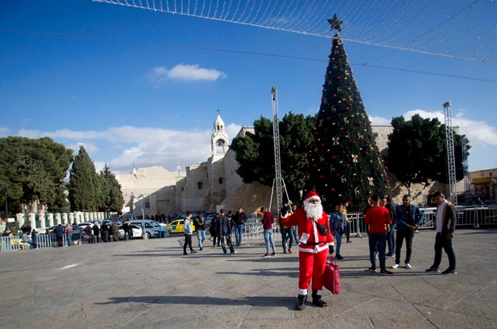 In this Thursday, Dec. 5, 2019, photo, a Palestinian wearing a Santa Claus costumes welcomes Christian visitors outside the Church of the Nativity, traditionally believed by Christians to be the birthplace of Jesus Christ, in the West Bank city of Bethlehem. (AP Photo/Majdi Mohammed)